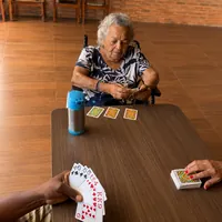 Idosa em cadeira de rodas jogando cartas com amigos no CEI - Centro Especializado para Idosos no Monte Castelo e